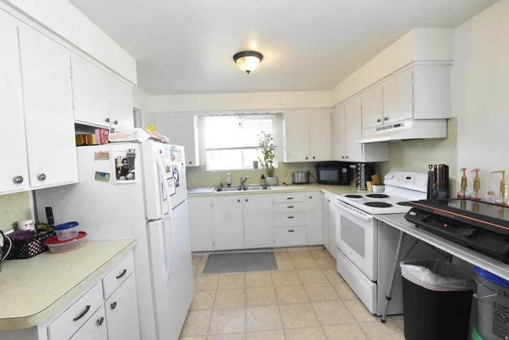 Kitchen featuring white cabinetry, light-toned countertops, a window over the sink, and tile flooring