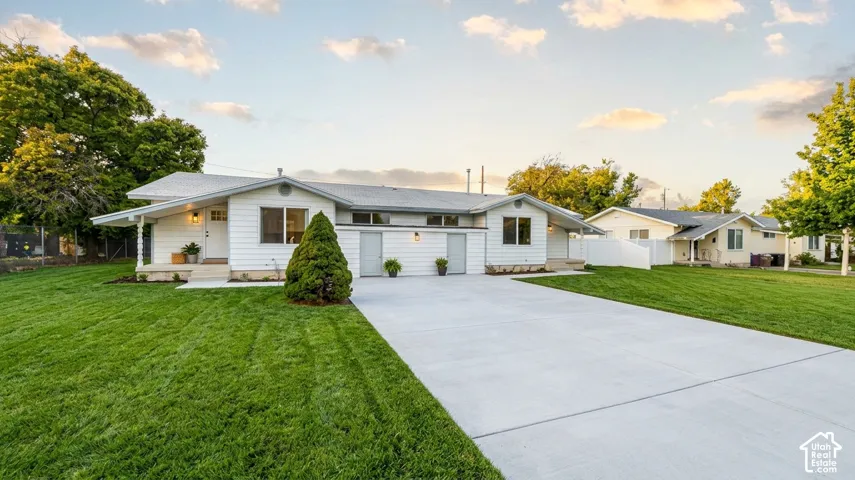 Single-story exterior featuring white horizontal siding, a light-toned shingle roof, expansive concrete driveway, and manicured lawn