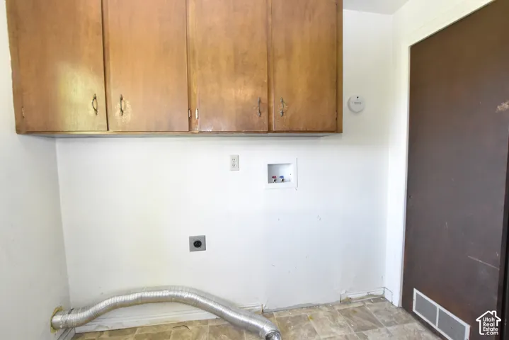 Utility space with wood-finish upper cabinetry, white walls, and vinyl flooring