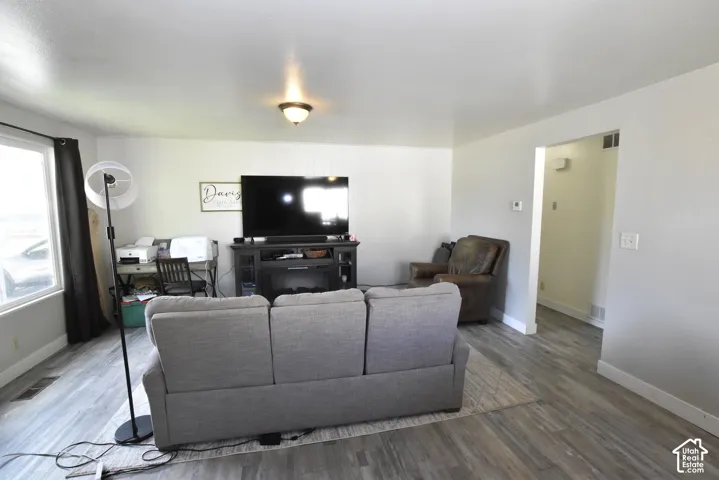 Spacious interior room featuring wood-finish flooring, light-toned walls, a large window, and an overhead light fixture