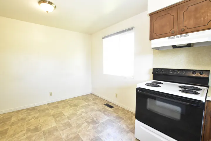 Kitchen area featuring a white range with black cooktop, wood-finish upper cabinetry, and a window with blinds