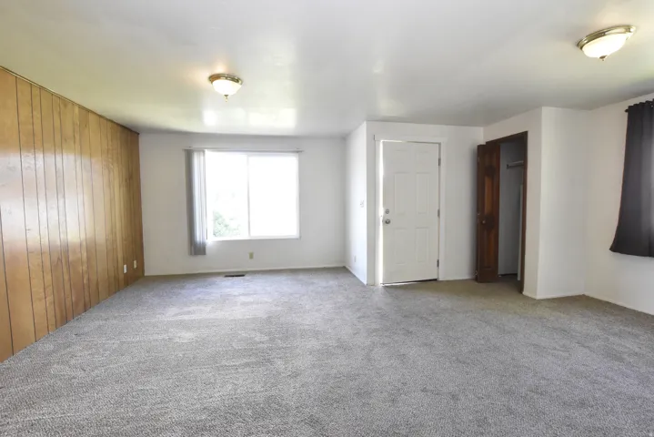 Spacious room featuring wood paneling, white painted walls, and gray carpet