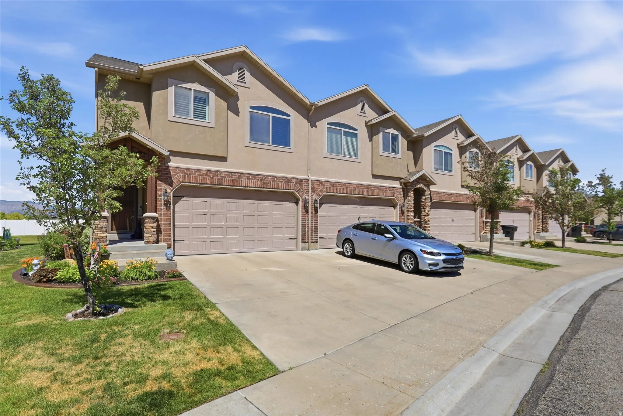 Contemporary townhome exterior featuring stucco and brick accents, an attached two-car garage, and a covered entry with stone pillars