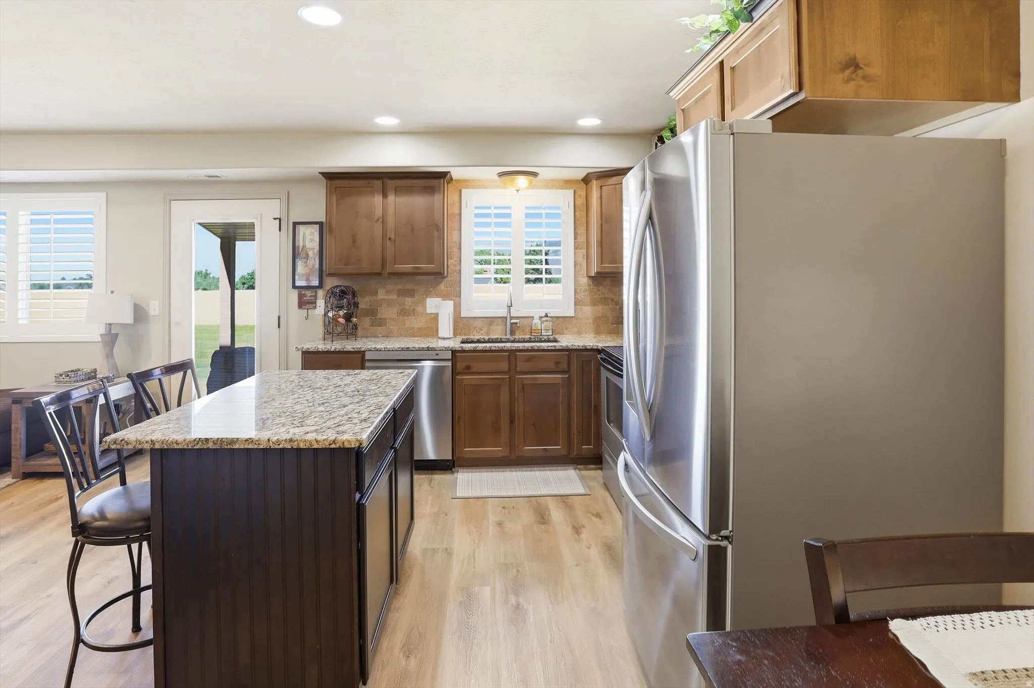 Kitchen featuring a central island with a granite countertop, wood-finish flooring, stainless steel appliances, and wood cabinetry