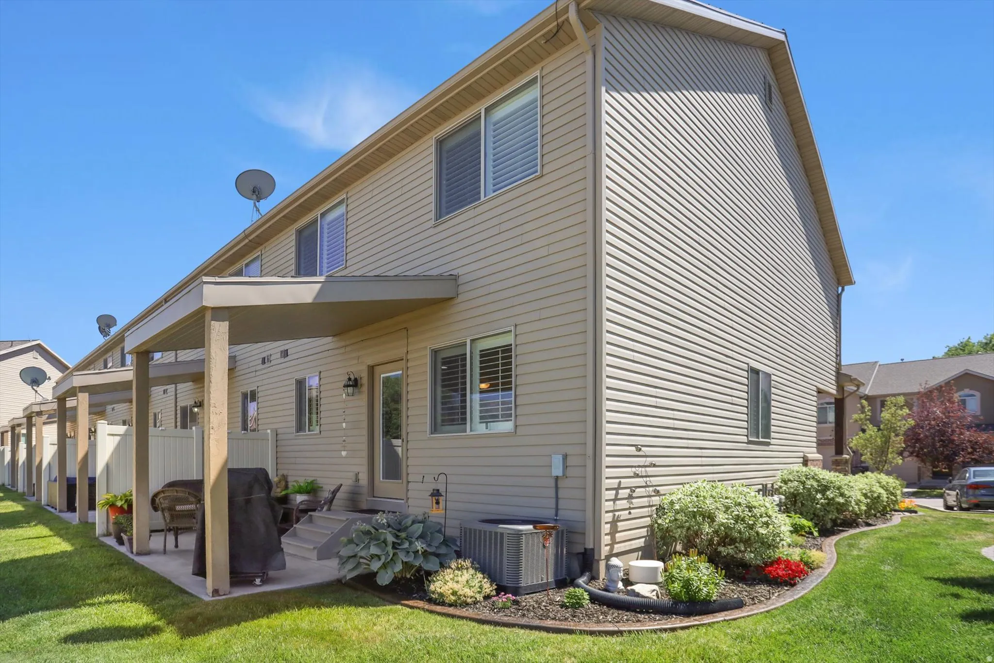 Rear exterior featuring a covered patio with concrete flooring, a manicured lawn, and established landscaping
