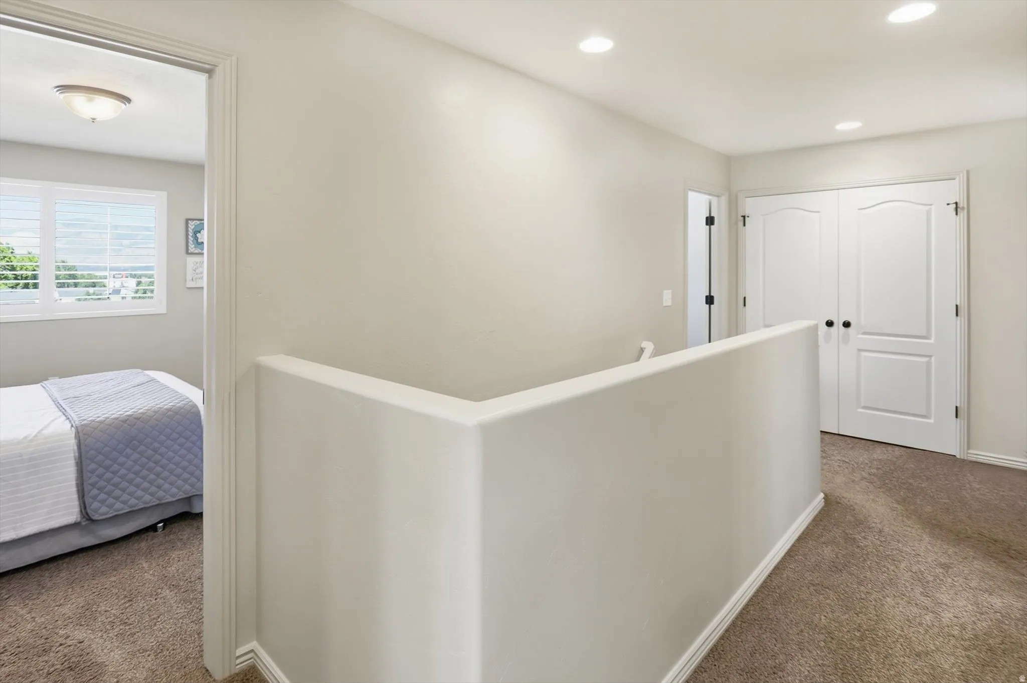 Upper-level landing featuring textured carpeting, recessed lighting, and a white half-wall