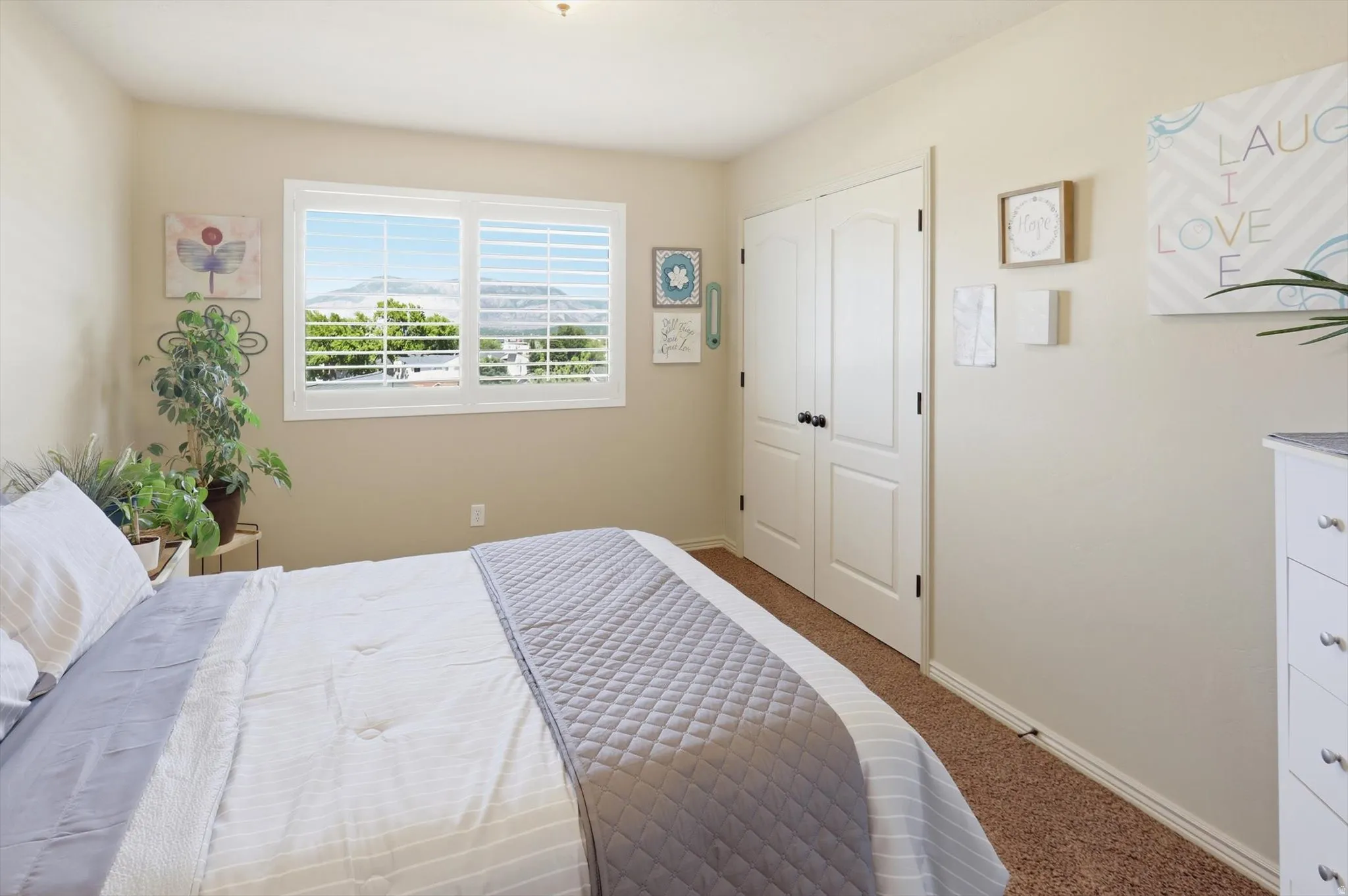 Bedroom featuring a window with white louvered shutters, offering a mountain backdrop