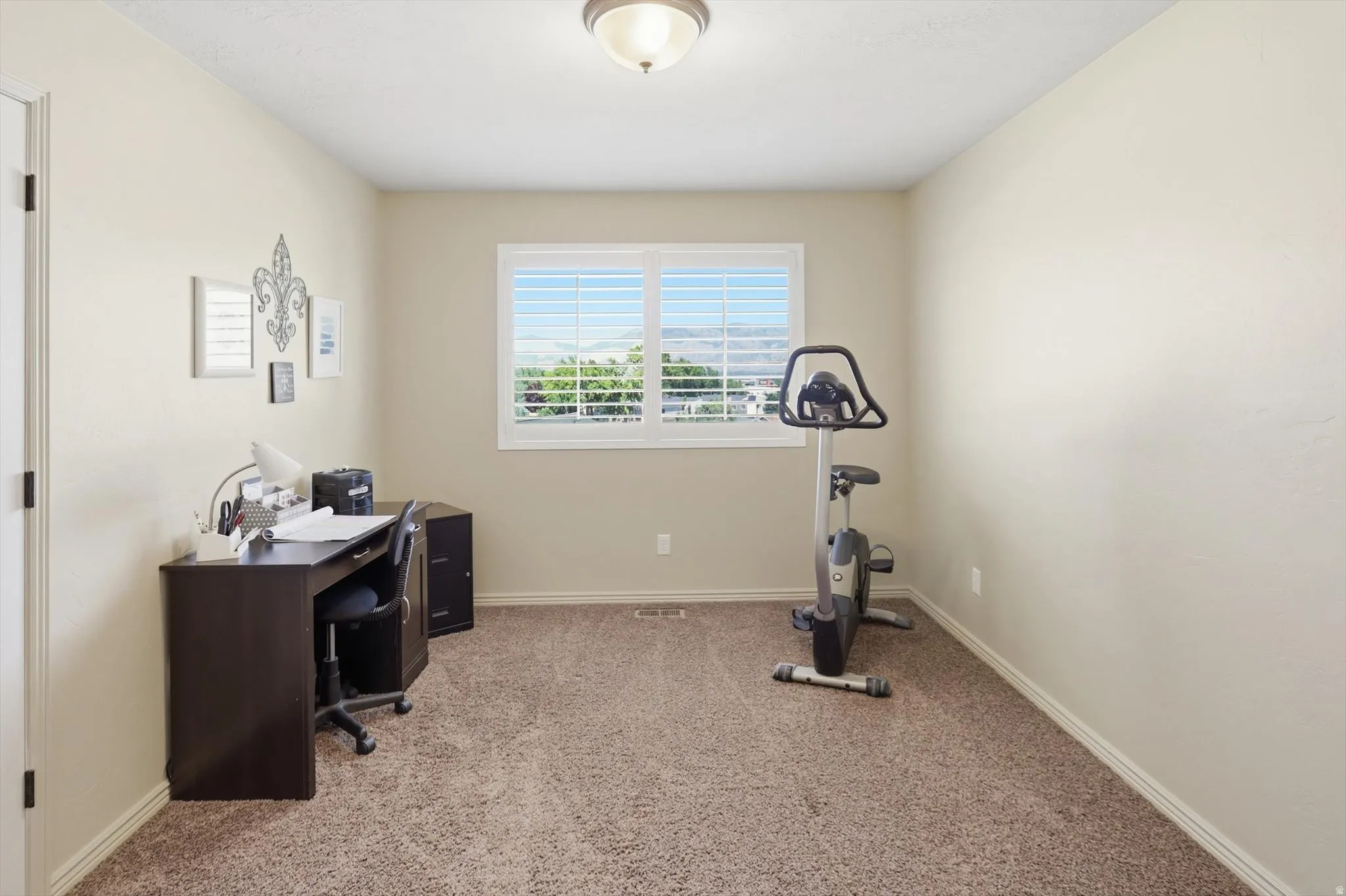 Neutral-toned room featuring light beige walls and a window with white plantation shutters