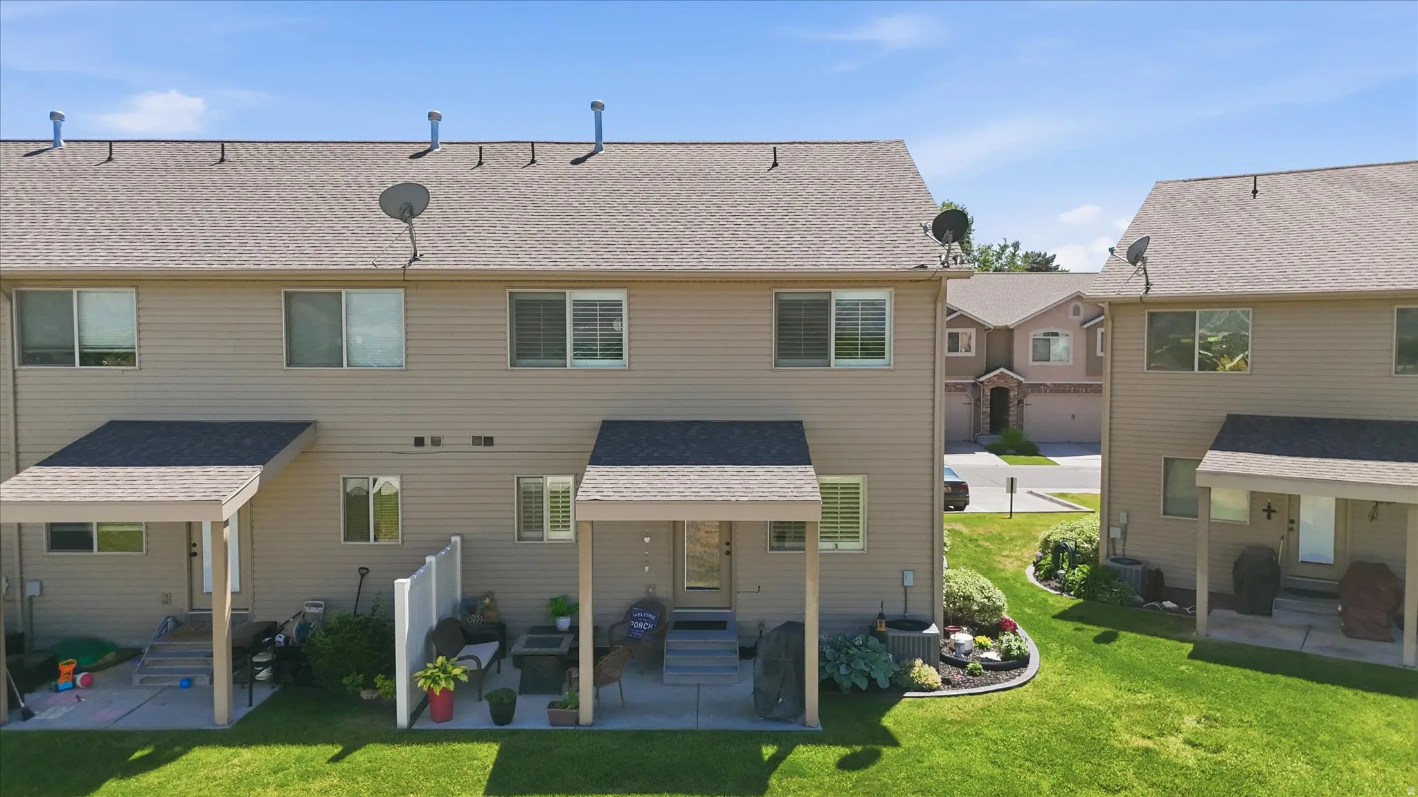 Rear exterior featuring a covered patio, manicured lawn, and landscaped garden beds
