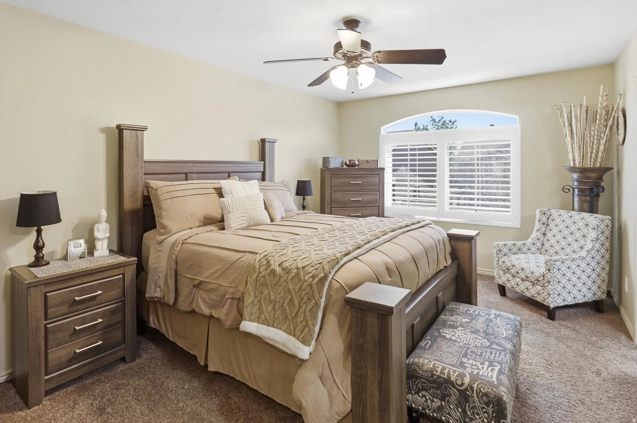 Carpeted bedroom featuring a ceiling fan with integrated lighting, a window with an arched transom, and white plantation shutters