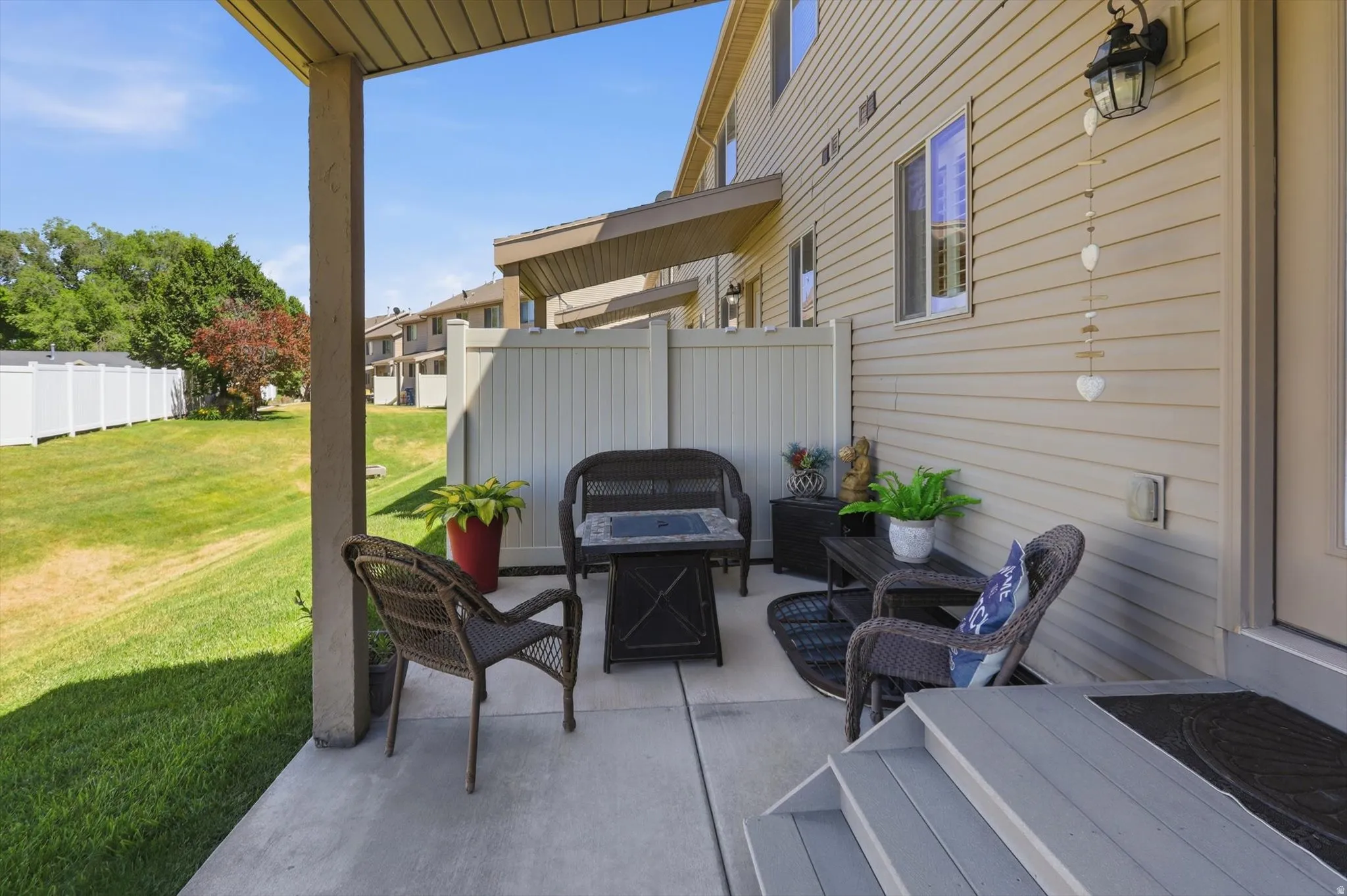 Covered concrete patio with siding exterior, privacy fence, exterior lighting fixture, and steps to a door
