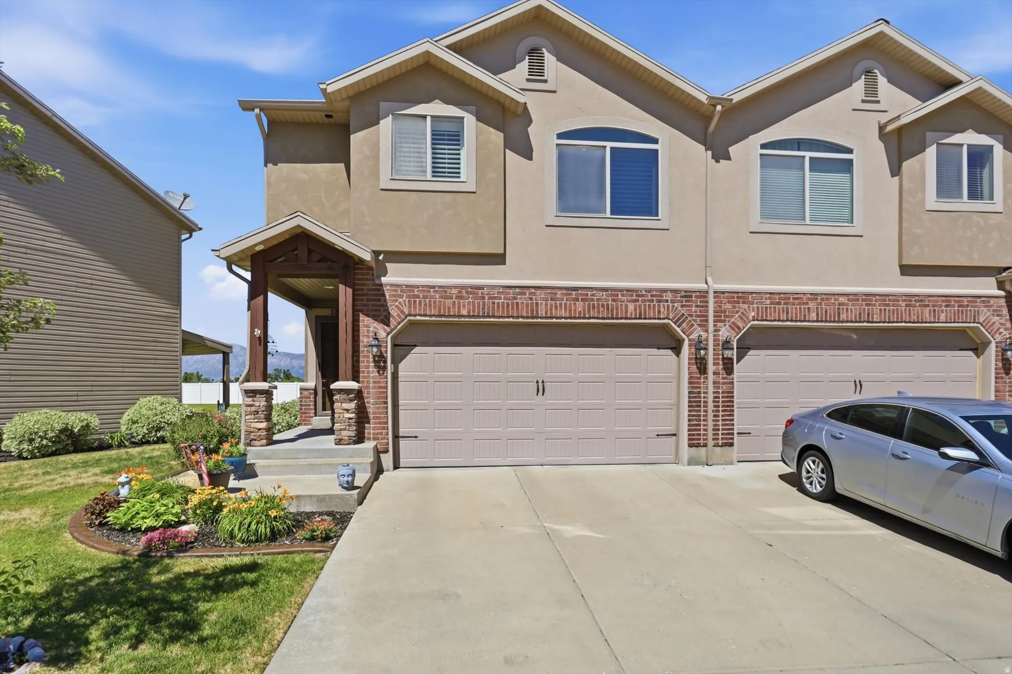 Stucco and brick exterior townhome featuring an arched entry porch with stone-clad columns, an attached two-car garage, and a concrete driveway