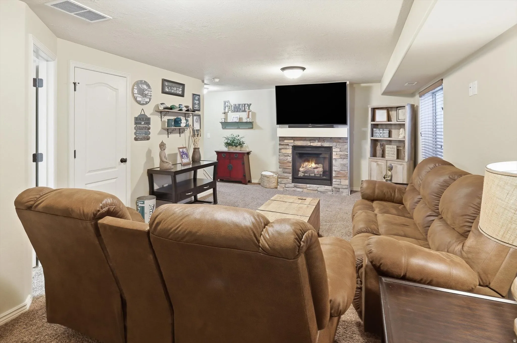 Carpeted living space featuring a stacked stone fireplace with a mounted television above