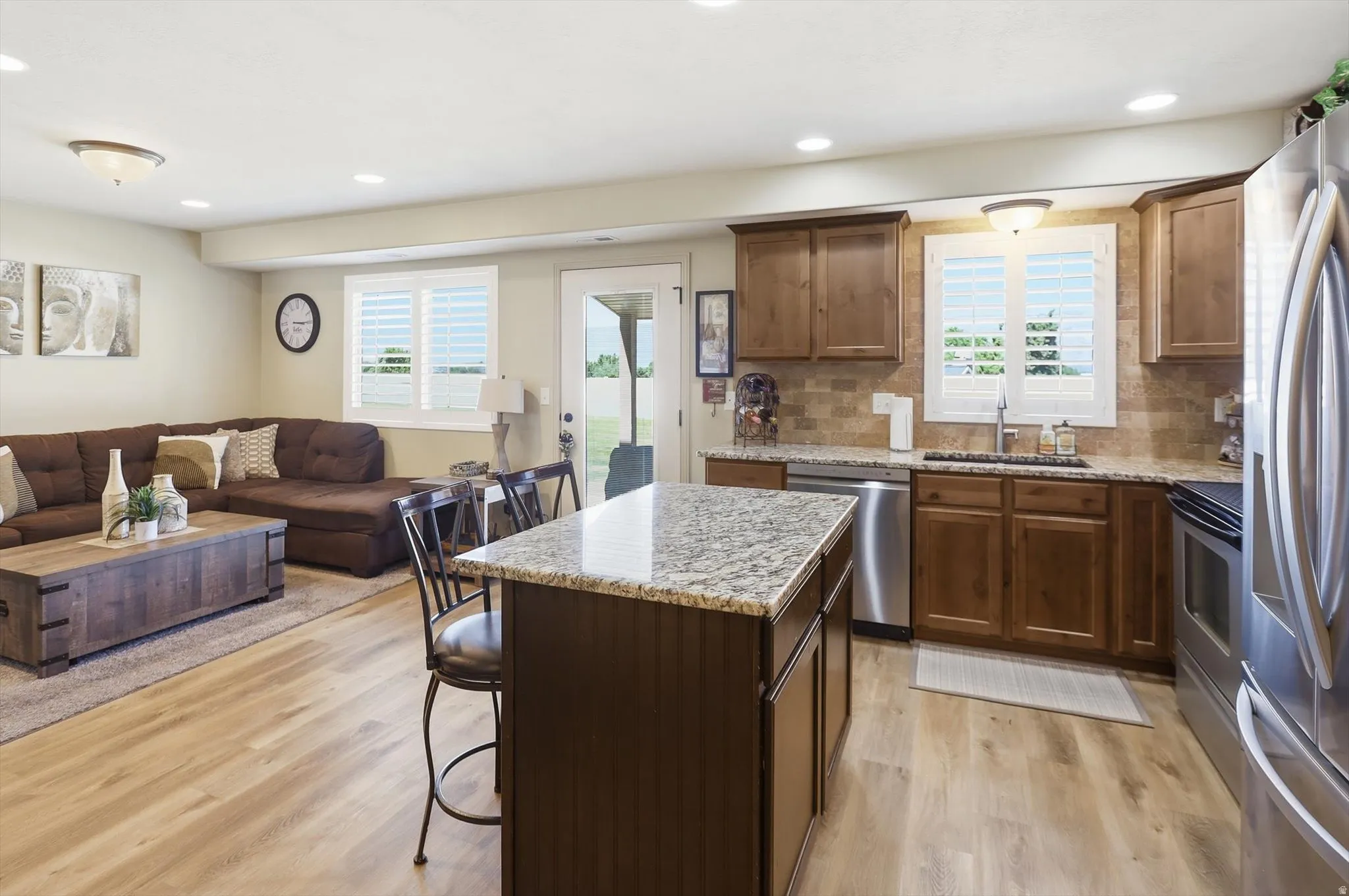 Open-concept living space featuring wood-finish flooring, a kitchen island with stone countertop, stainless steel appliances, recessed lighting, and a glass-paned exterior door
