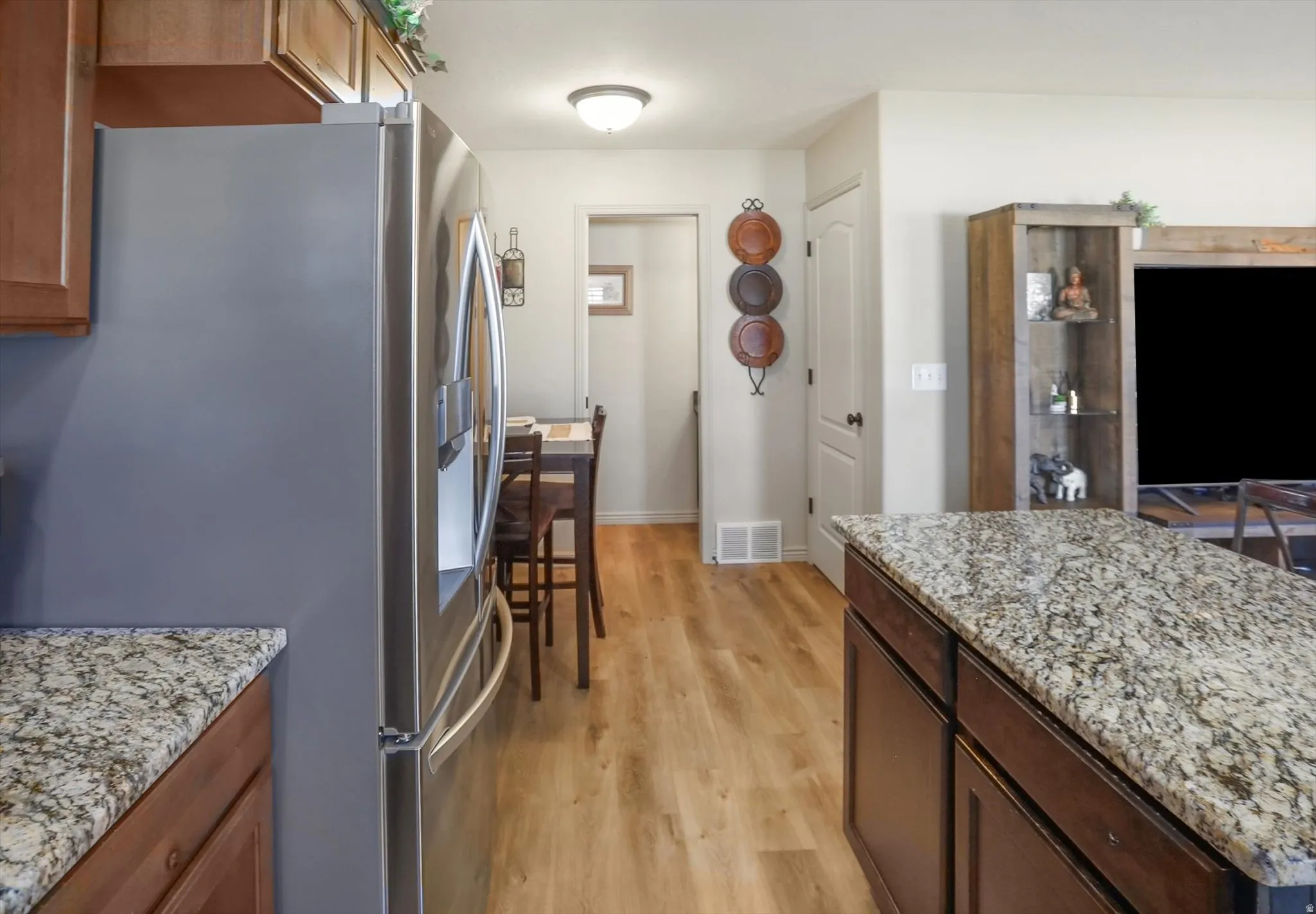 Kitchen featuring a stainless steel refrigerator, wood-finish flooring, and granite countertops on both the perimeter cabinetry and the island