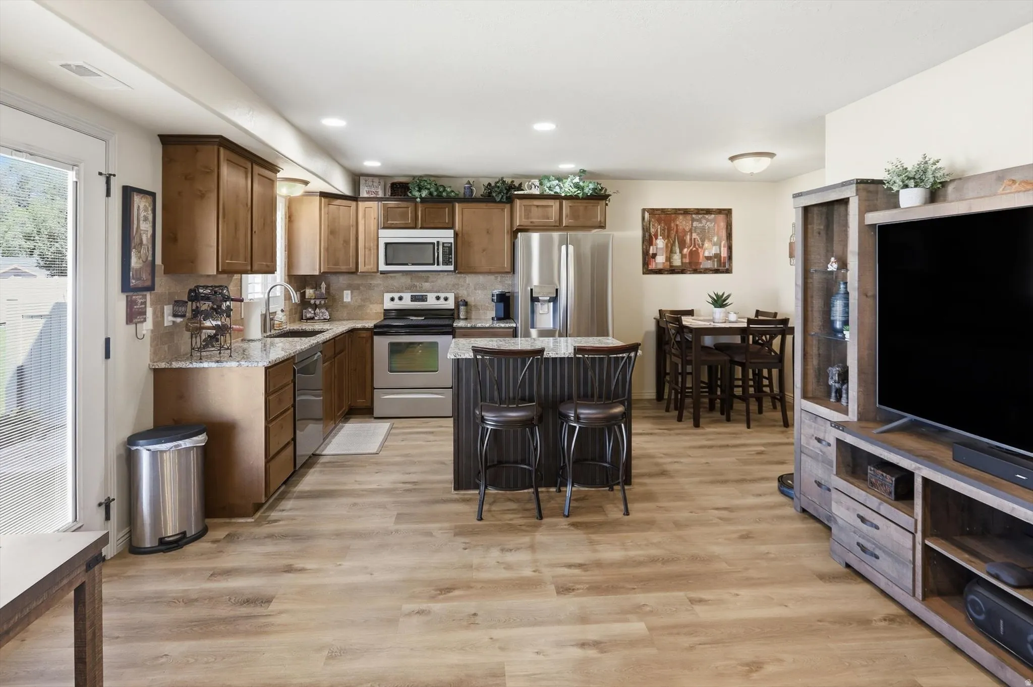Open-concept living space featuring wood-finish flooring, a kitchen with wood cabinetry and stainless steel appliances, granite countertops, and a central kitchen island