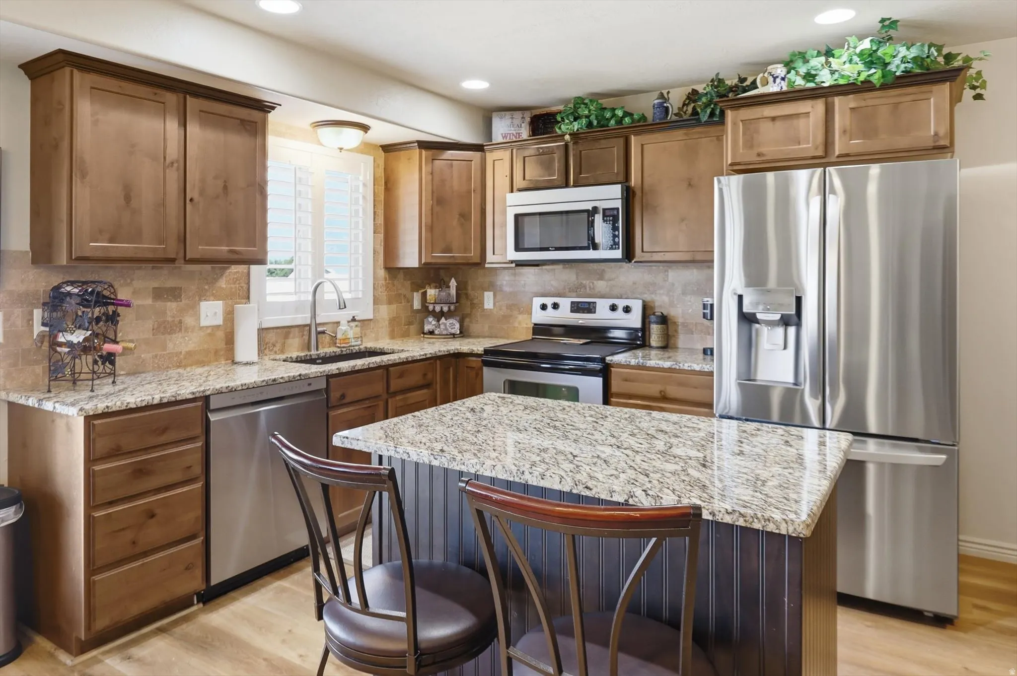 Kitchen featuring wood-finish cabinetry, granite countertops, stainless steel appliances, and a central island with counter seating