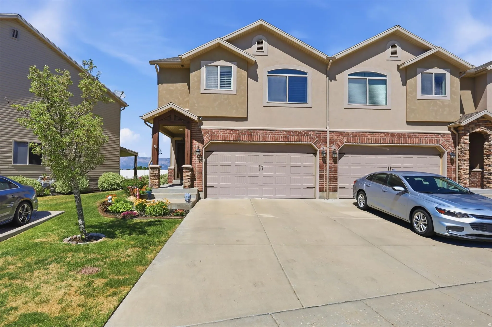 Contemporary townhome exterior featuring a two-car garage, brick accents, stucco siding, a covered entry, and a landscaped front yard
