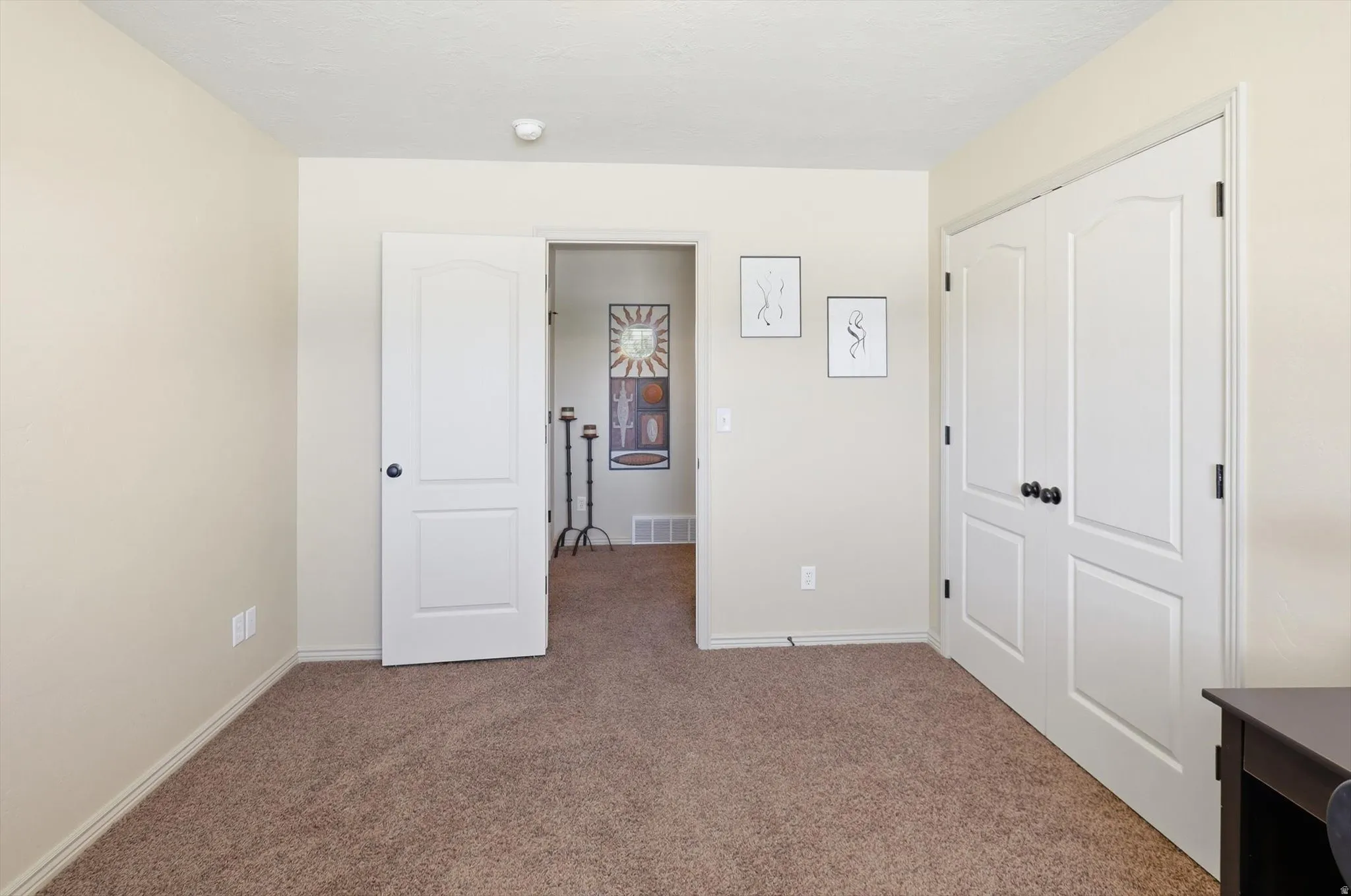Carpeted interior room featuring neutral wall tones, white trim, a white interior door with dark hardware, and a white bi-fold closet door with dark hardware