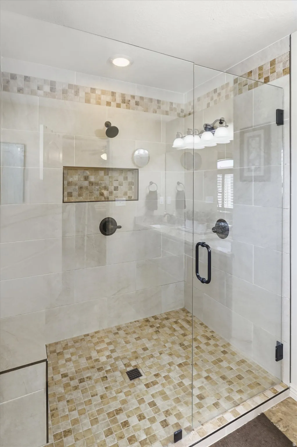 Glass-enclosed shower featuring large format wall tiles, a mosaic tile floor, and a recessed shower niche