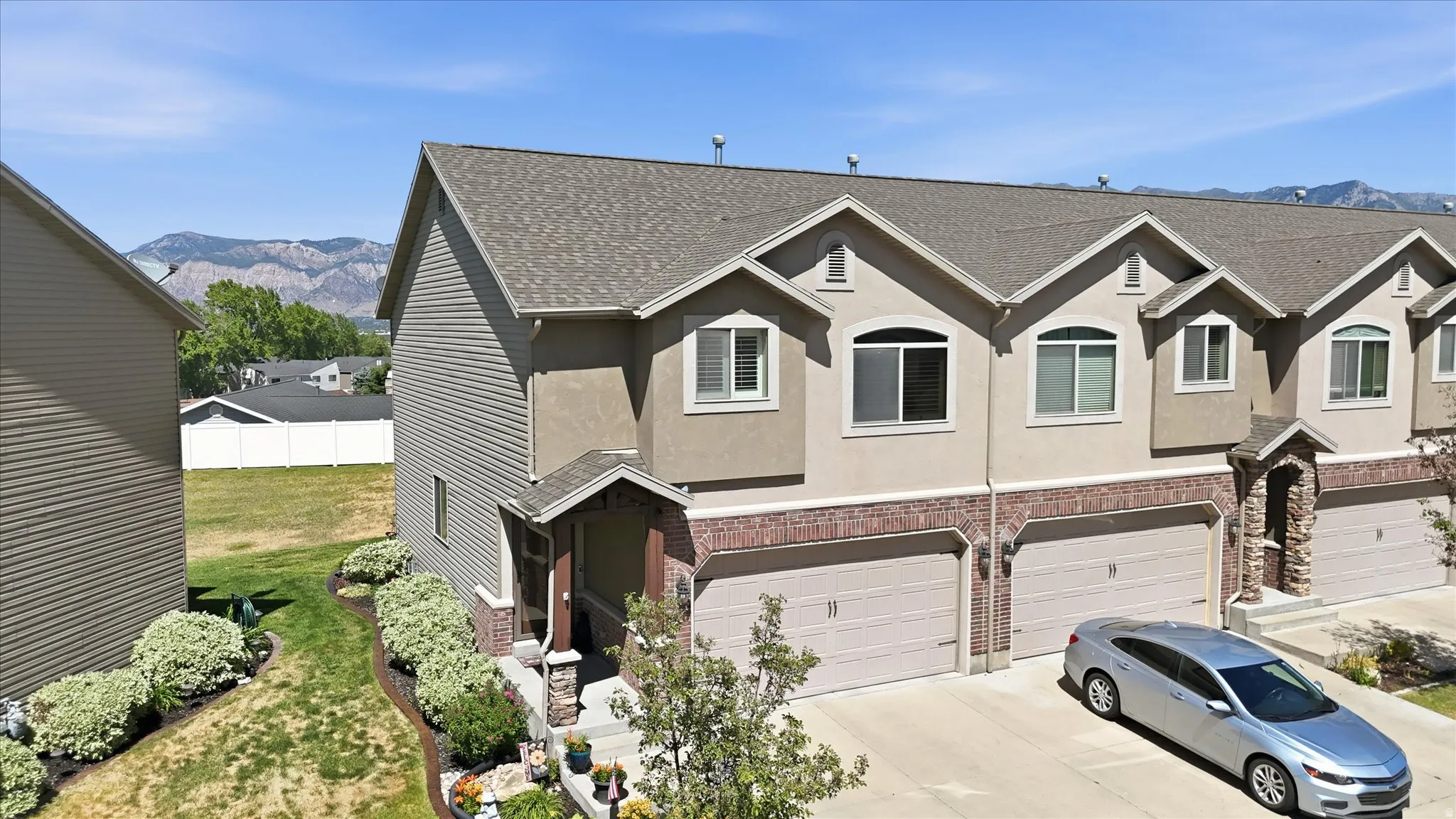 Multi-level townhouse with a two-car garage featuring a tan exterior, stone accents, and an arched entry