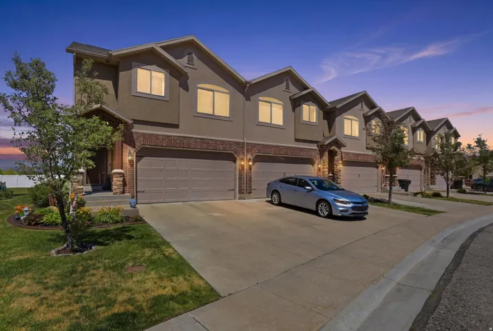 Townhome exterior featuring a stucco and brick facade, arched windows, an attached two-car garage, concrete driveway, and landscaped front yard with mature trees