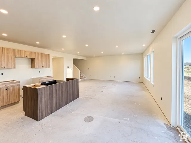 Recessed lighting, wood-finish cabinetry, central island with wood-finish paneling, multiple windows, and a sliding glass door