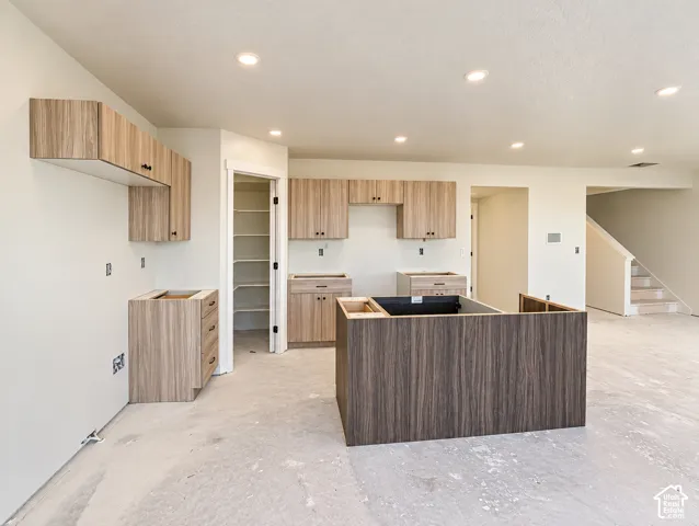 Recessed lighting throughout, two-tone wood-finish cabinetry, an integrated kitchen island, and a pantry with built-in shelving
