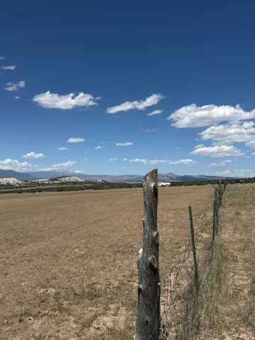 Expansive open field bordered by a rustic wooden fence and wire fencing, offering distant mountain scenery