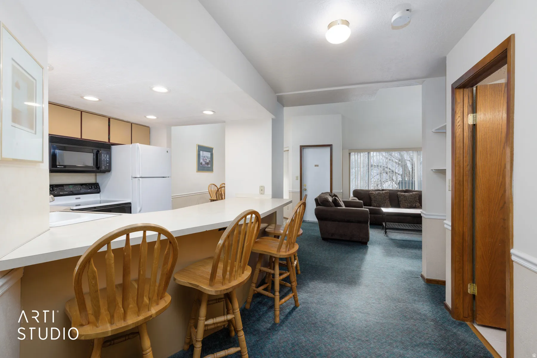 Kitchen bar seating with a light-toned countertop, a full suite of white and black appliances, light wood-tone cabinetry, and recessed lighting
