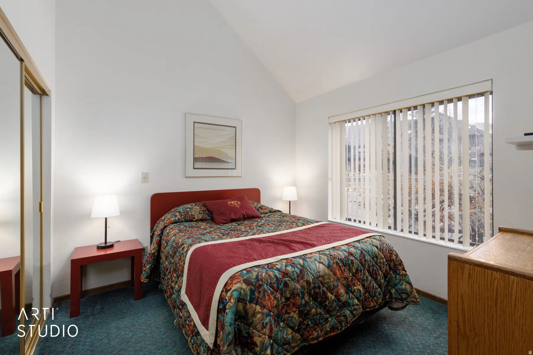 Room featuring a vaulted ceiling, large window with vertical blinds, and wall-to-wall carpeting