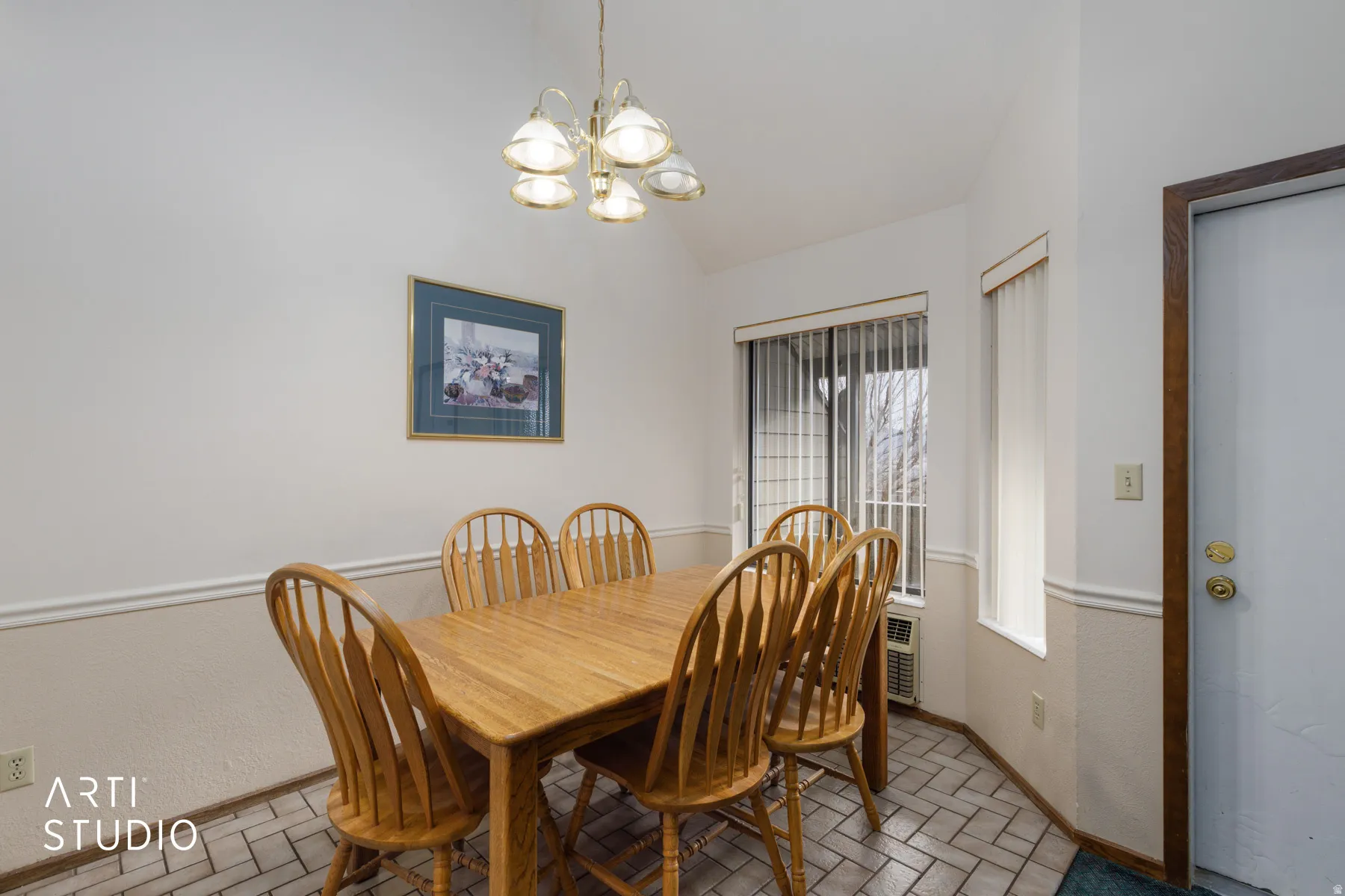 Dining area featuring a vaulted ceiling, patterned tile flooring, and wainscoting