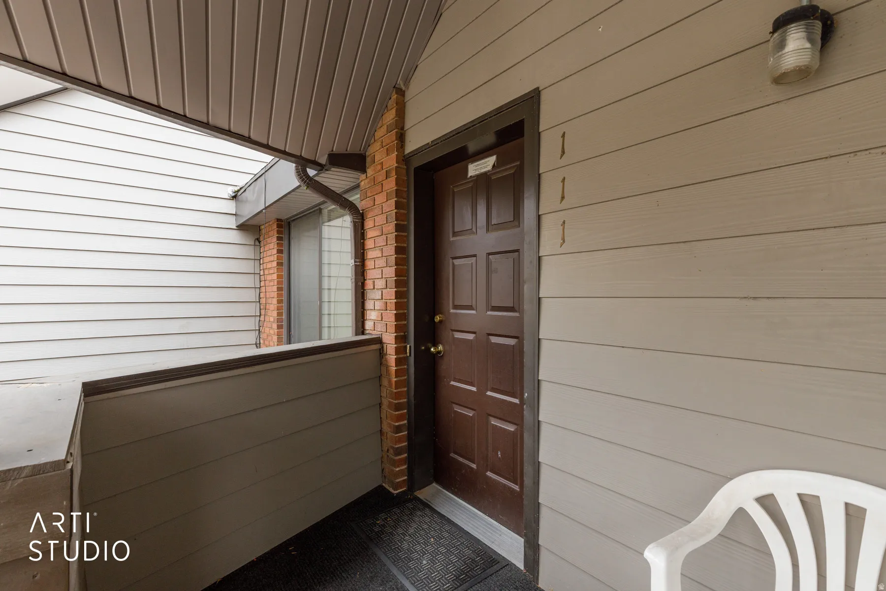 Entryway featuring a paneled door with brass hardware, brick accents, and horizontal siding