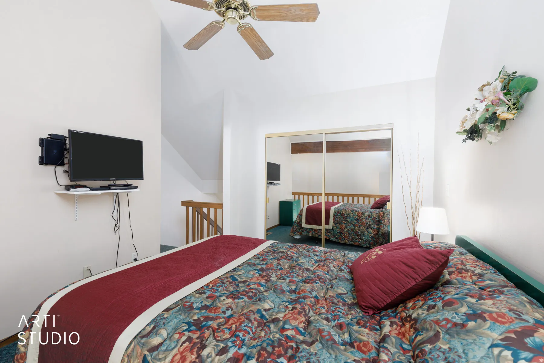 Vaulted ceiling bedroom with a ceiling fan, wall-mounted television, and mirrored closet doors