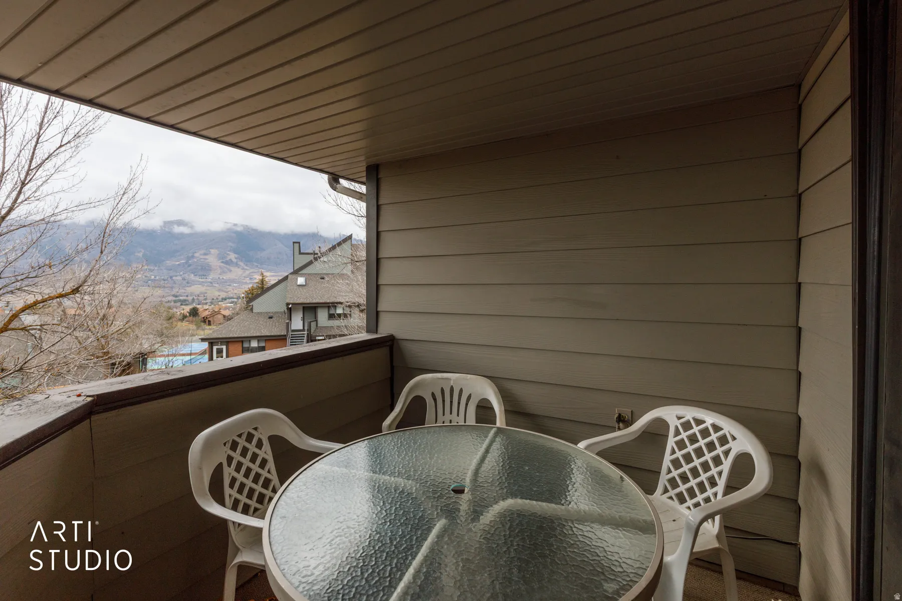 Covered balcony with mountain scenery, featuring tan horizontal siding and a dark trim railing