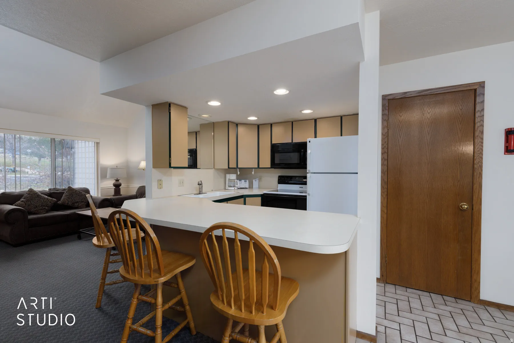Kitchen featuring a breakfast bar with seating, white countertops, tan cabinetry, and white and black appliances