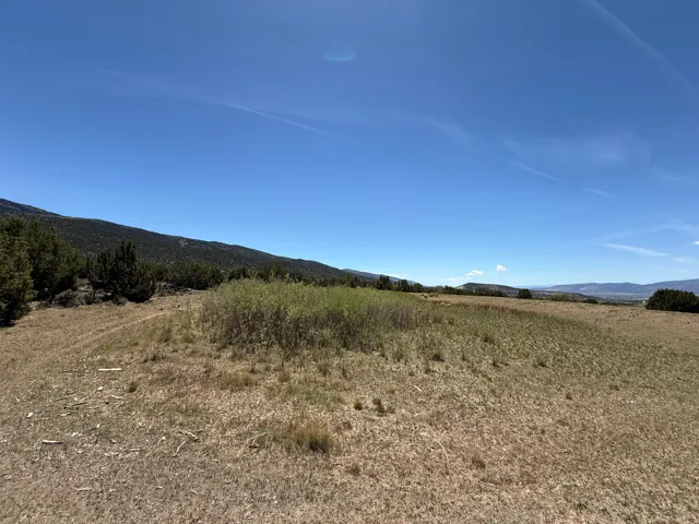 Expansive property featuring varied ground cover, distant mountain ranges, and a bright blue sky