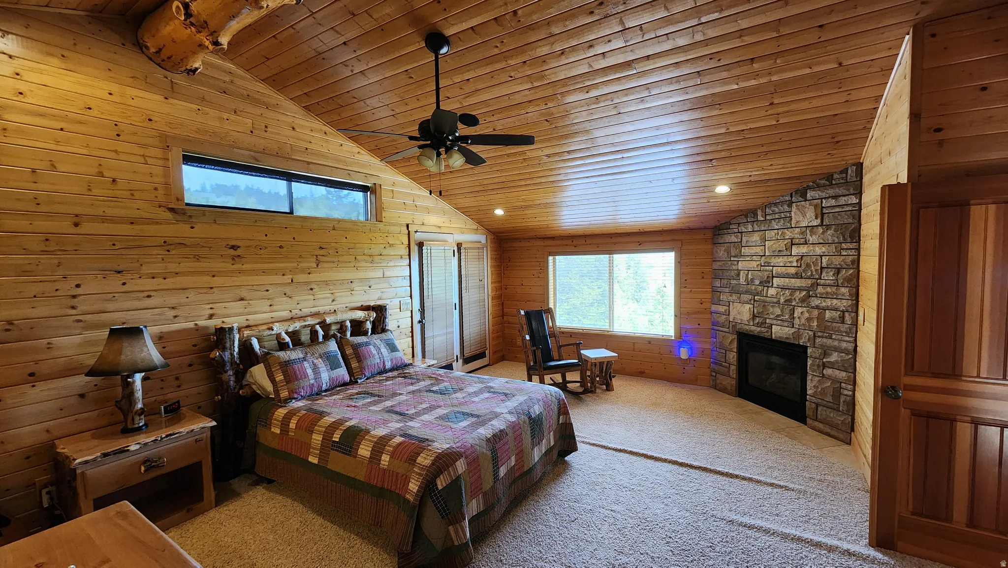 Spacious room featuring extensive wood paneling, a stone-faced fireplace, vaulted wood-finish ceiling, and multiple windows