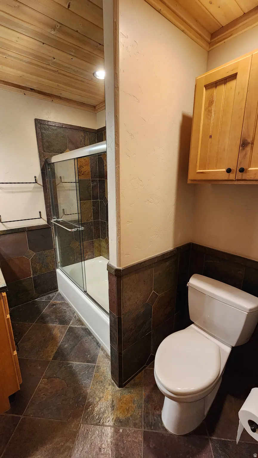 Bathroom featuring natural wood plank ceiling, full bath with glass enclosure, wall-mounted natural wood cabinetry, and slate-style floor and wall tile