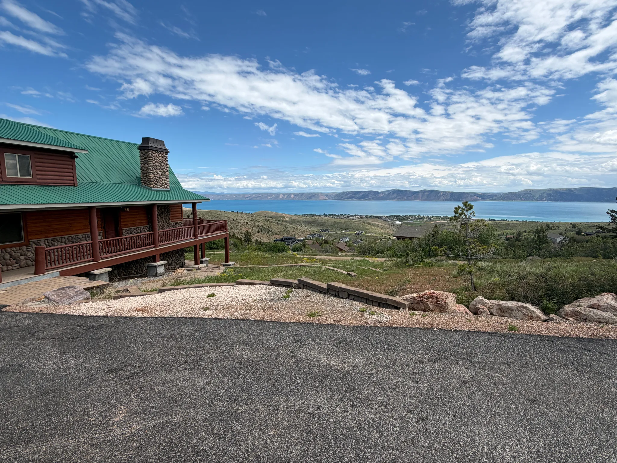 Log cabin style home featuring a green roof, stone chimney, and an expansive covered porch