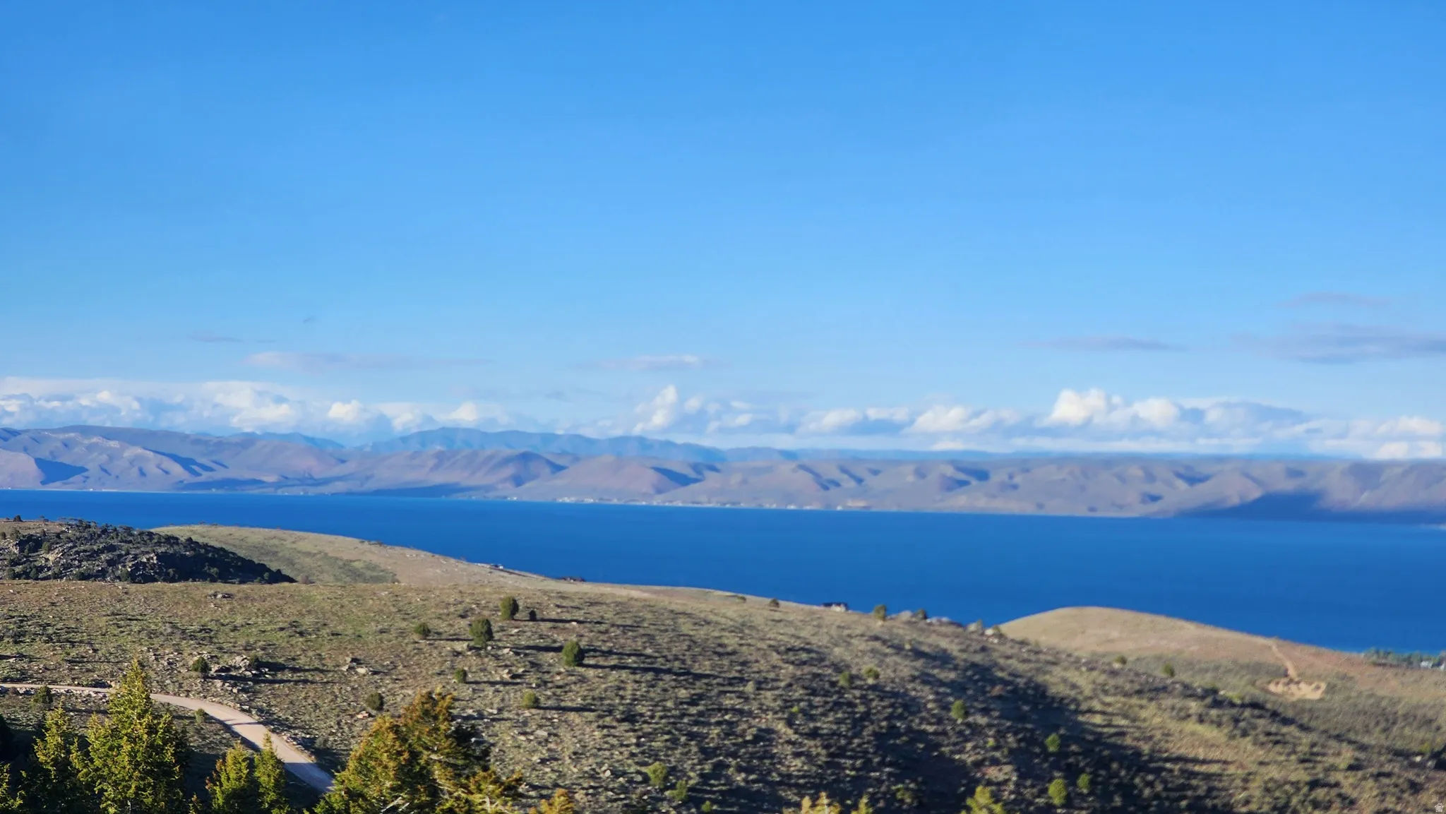 Expansive landscape featuring a large body of water bordered by distant mountains and rolling hills