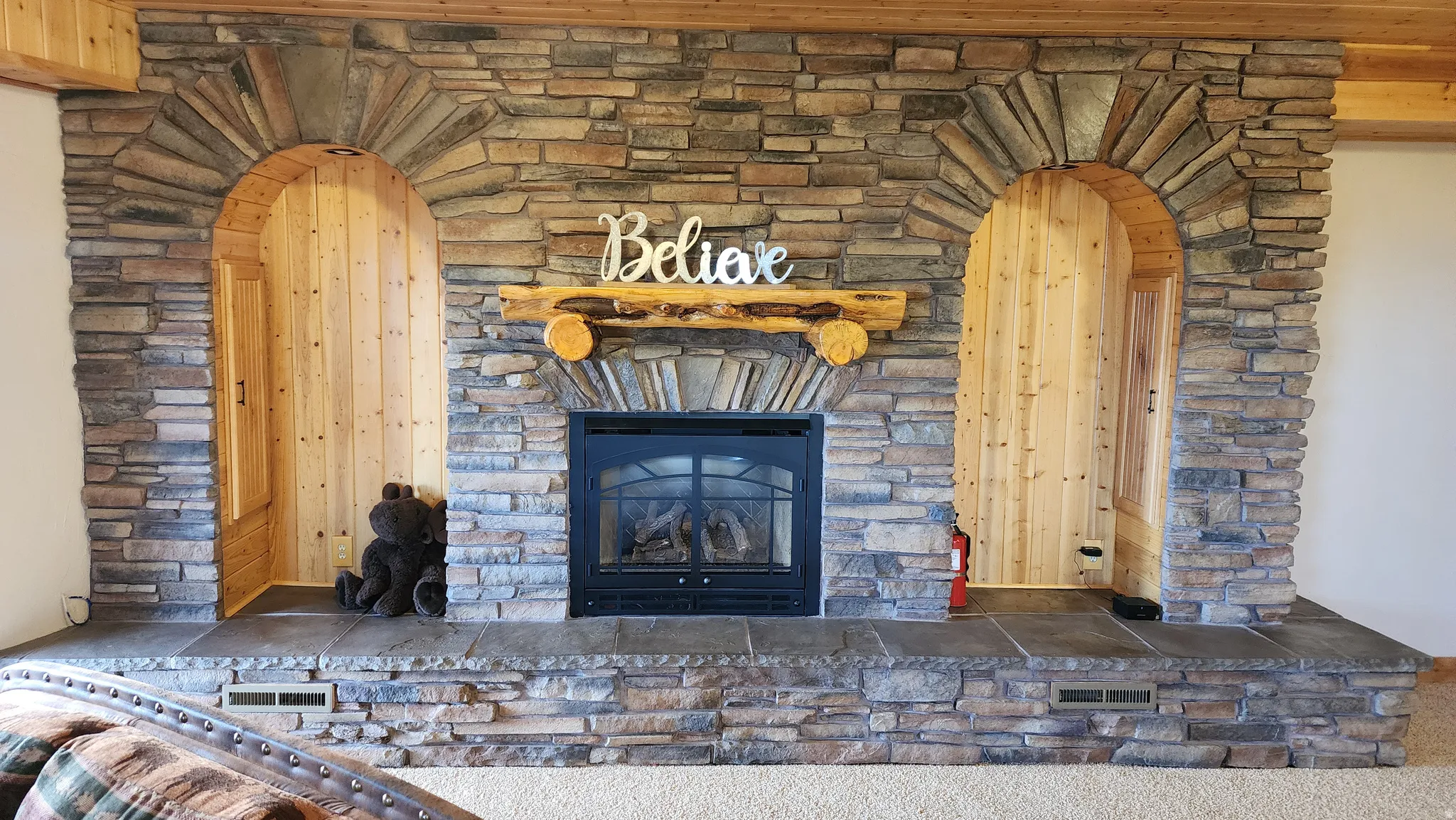 Stone-clad fireplace featuring a gas insert, a log mantel, and two arched alcoves with wood paneling