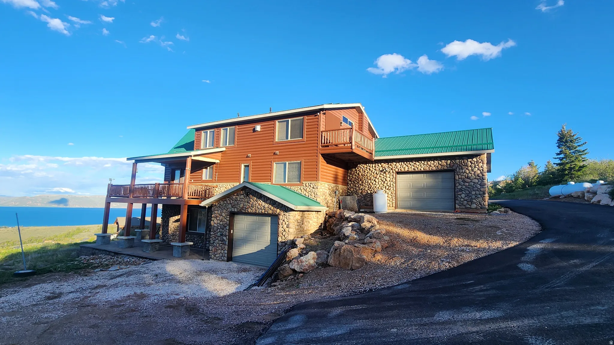 Stone and wood-sided residence featuring multiple outdoor decks, a green metal roof, and an attached two-car garage