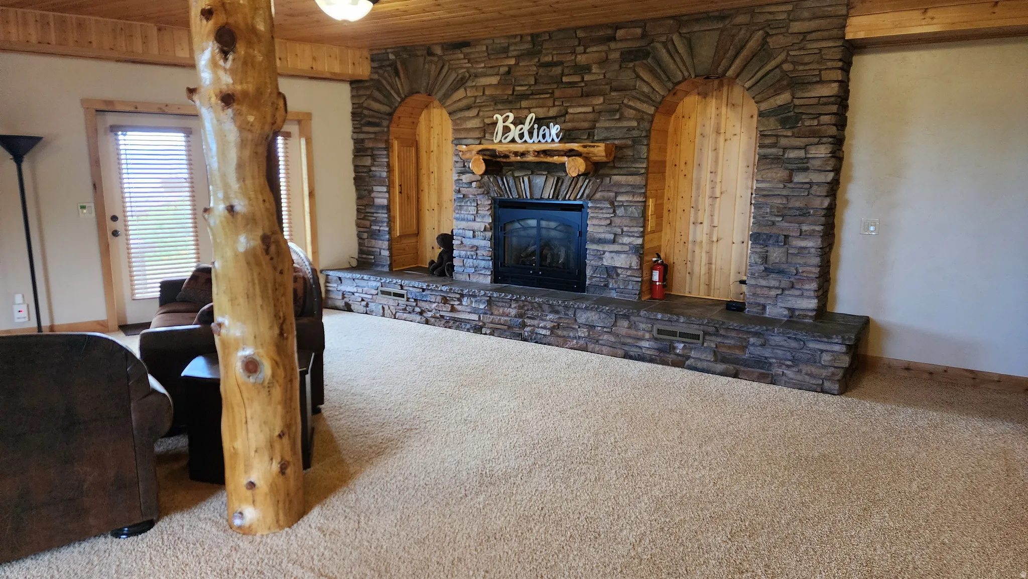 Spacious room featuring a prominent stone fireplace with a wood mantle and two arched alcoves, one with wood paneling