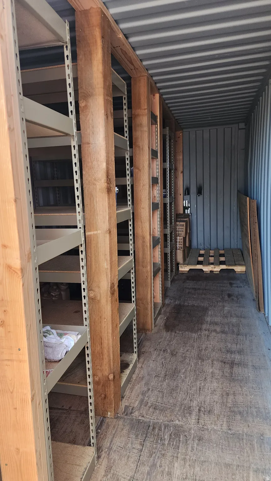 Interior storage unit featuring extensive shelving, corrugated metal walls, wood-finish flooring, and natural wood support beams