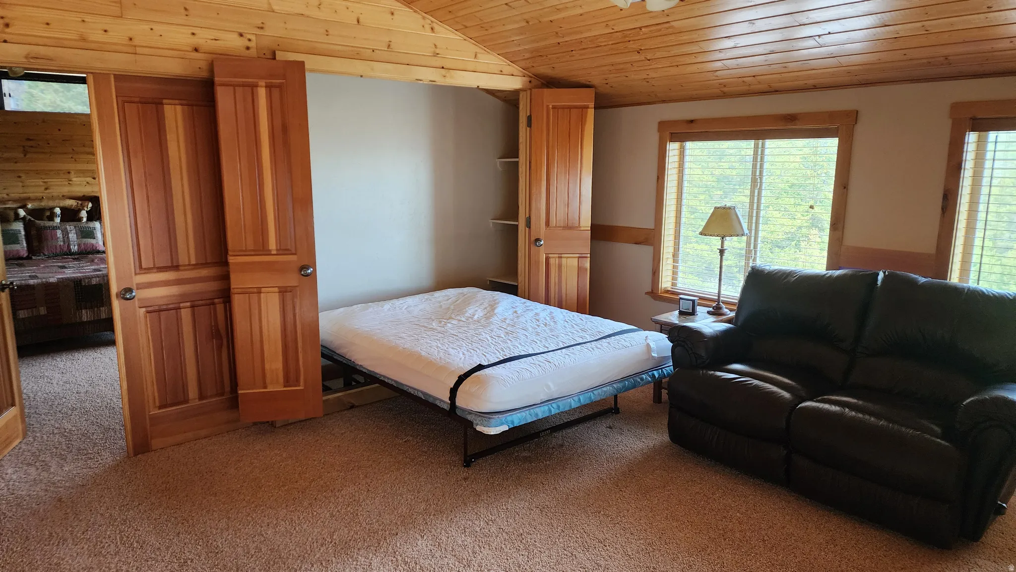 Warm wood-paneled ceiling and walls, recessed shelving, and a pair of windows with horizontal blinds