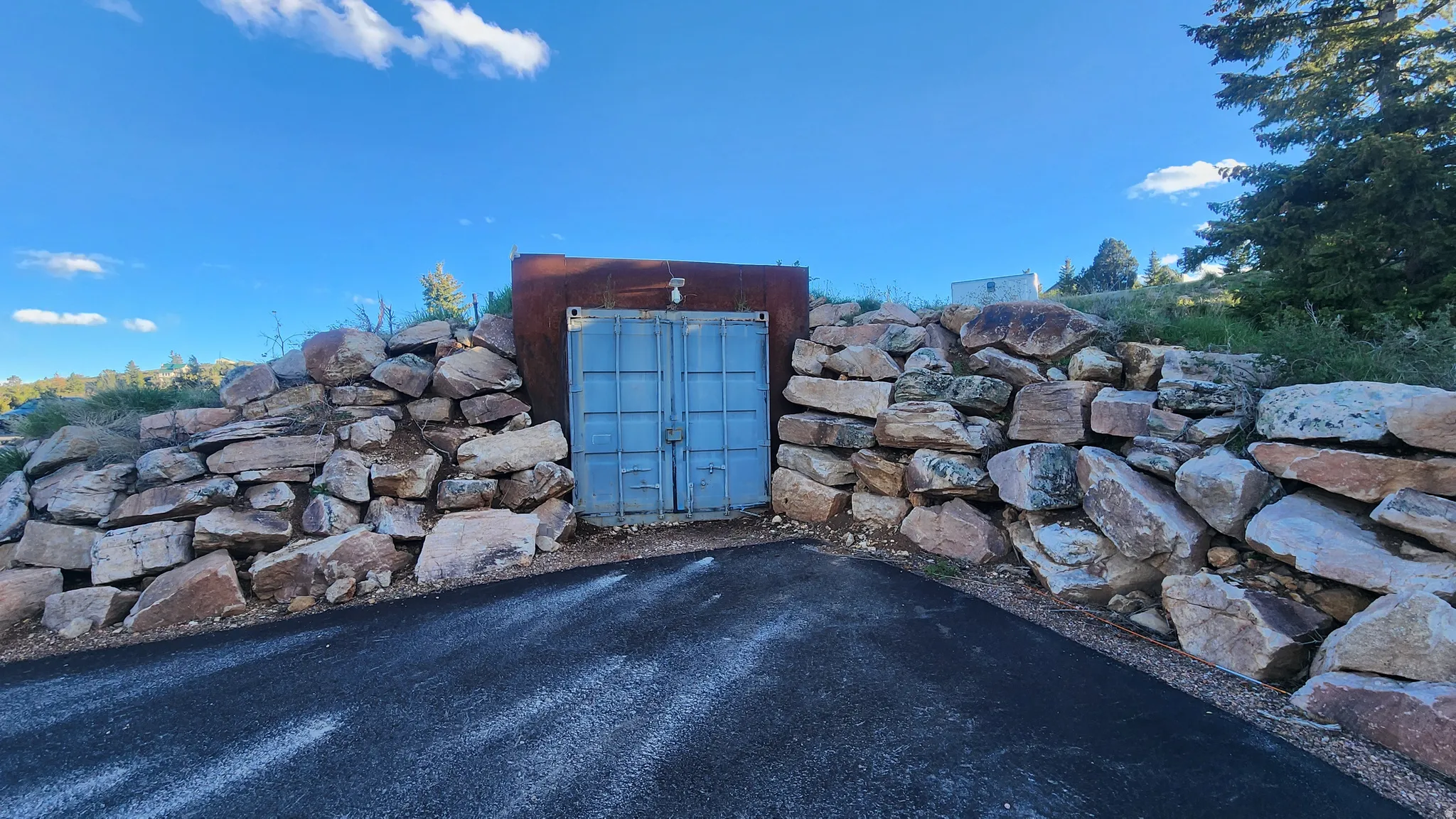 Blue metal double doors with a rusted metal frame, set into a retaining wall constructed of natural stones