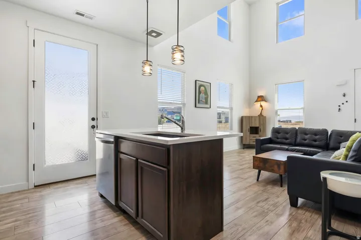 Vaulted ceilings, wood-finish flooring, kitchen island with sink, white quartz countertop, and pendant lighting