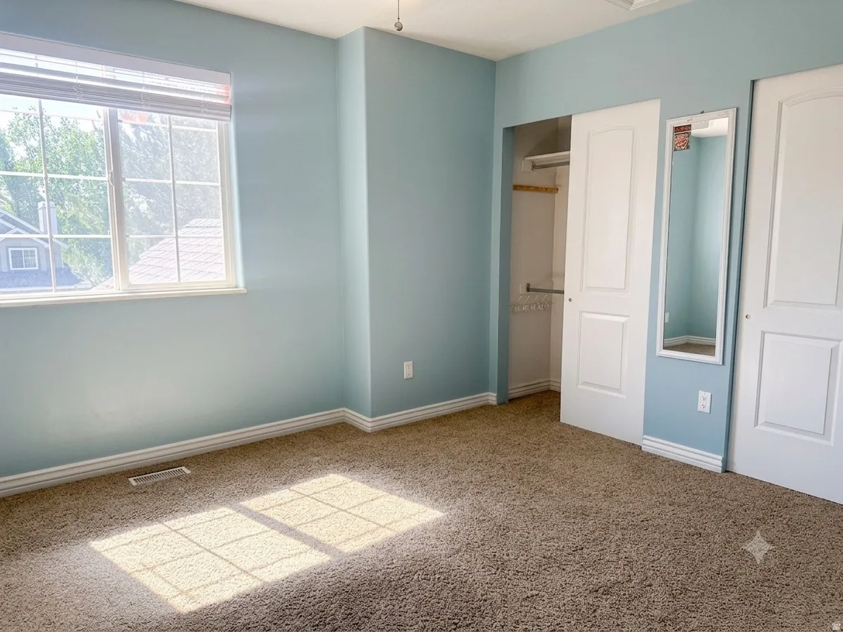 Carpeted room featuring a large window, white blinds, and two sliding closet doors