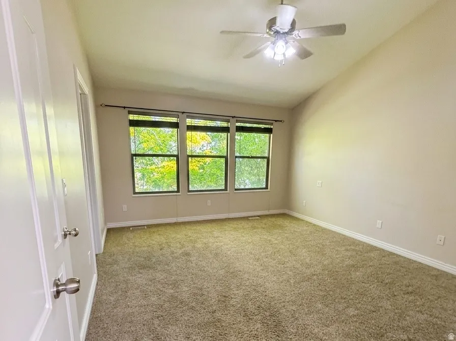Spacious main primary room featuring plush carpeting, three large windows, a ceiling fan with integrated lighting, and white paneled doors